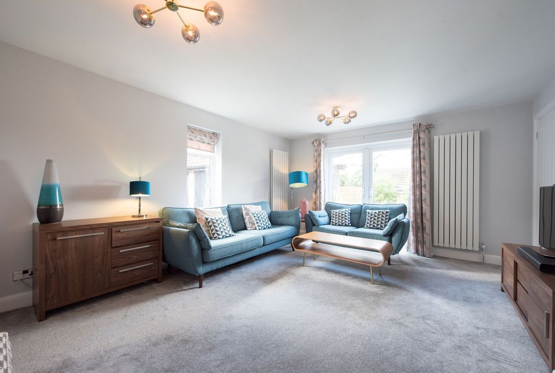 Living room with blue sofas, gray carpet, wood furniture, and white walls.