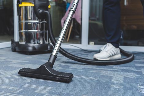 Person vacuuming blue patterned carpet with a vacuum cleaner.
