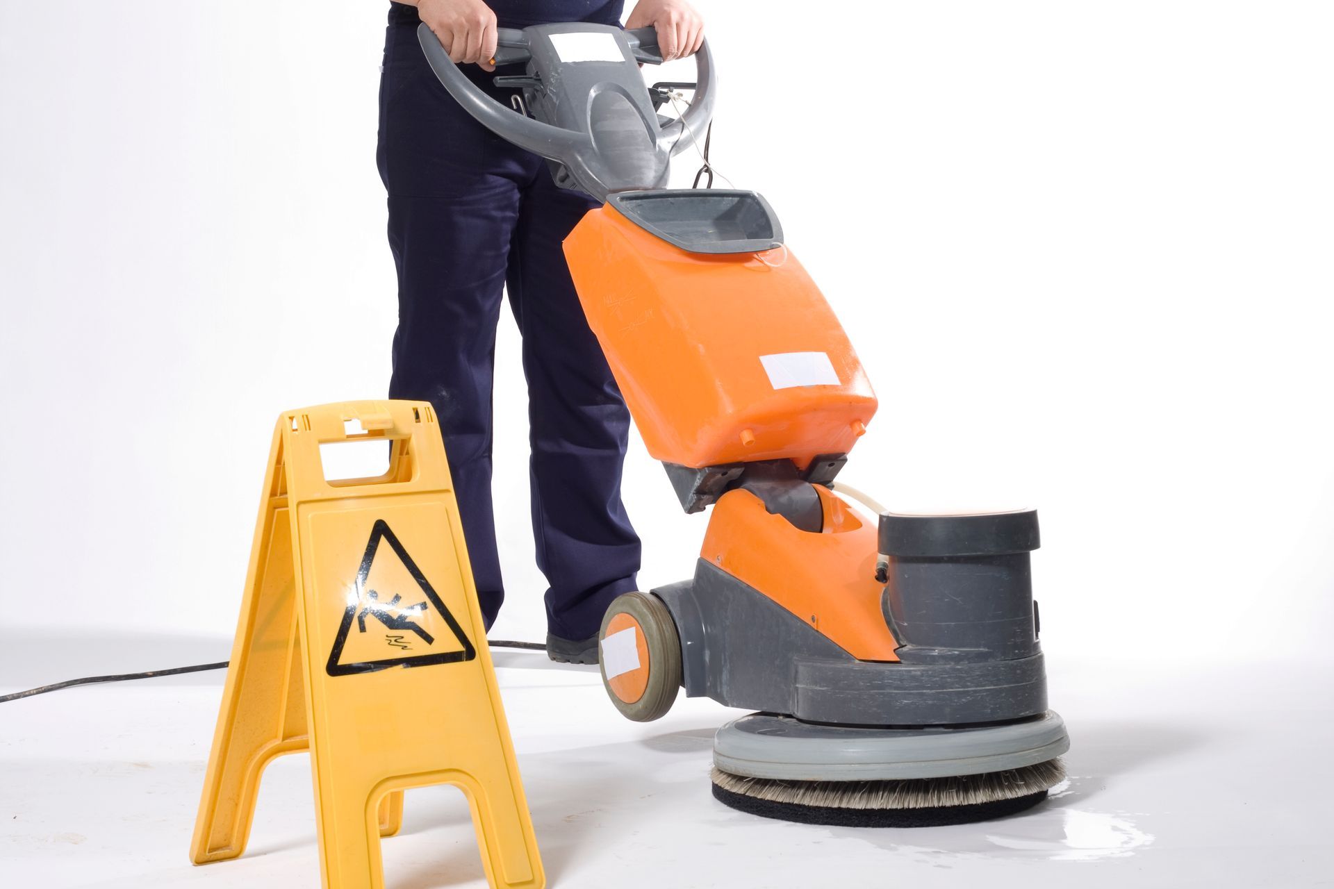 Person operating a floor buffer next to a yellow caution sign on a white floor.