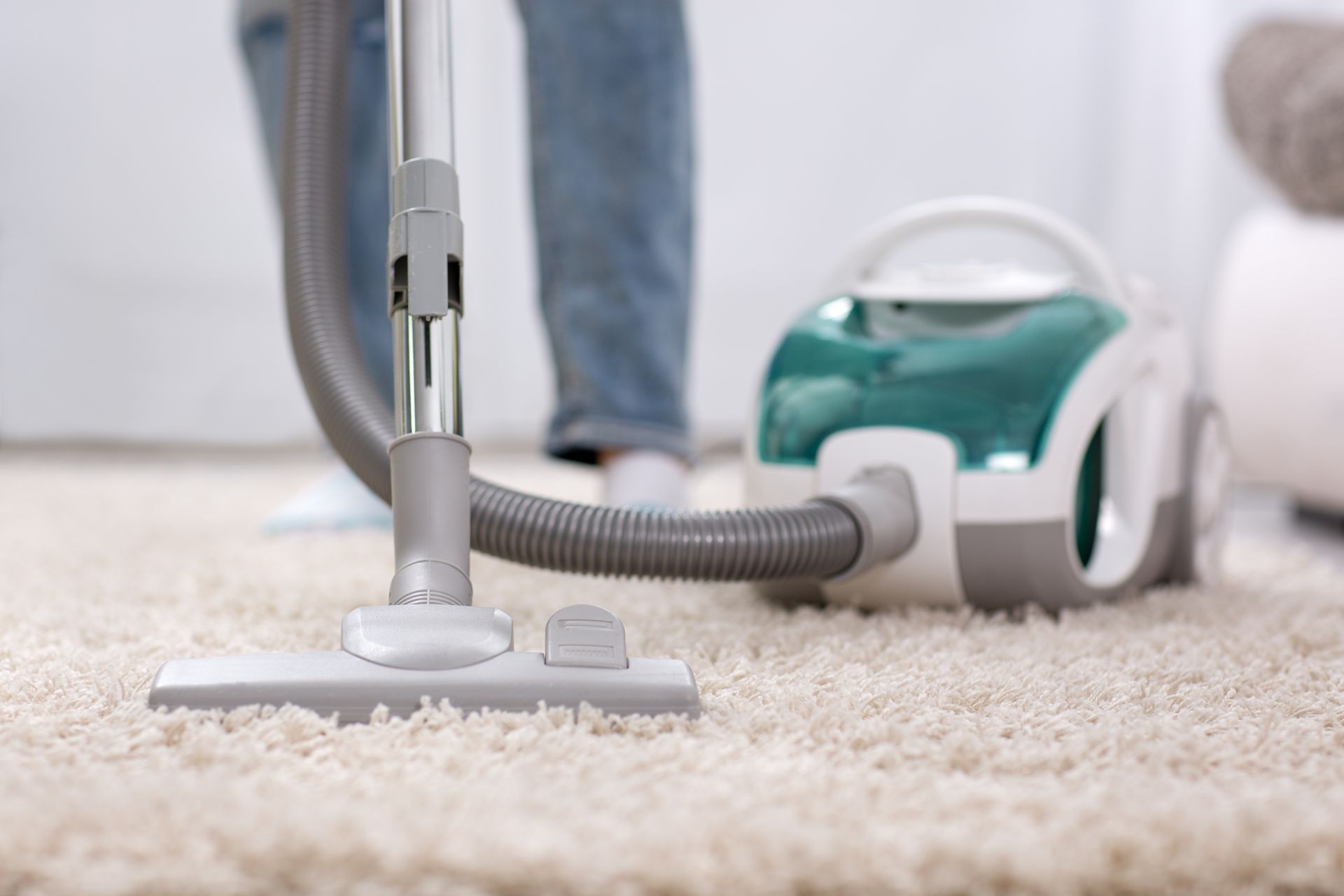 Person vacuuming a cream-colored rug with a green and white vacuum cleaner in a room.