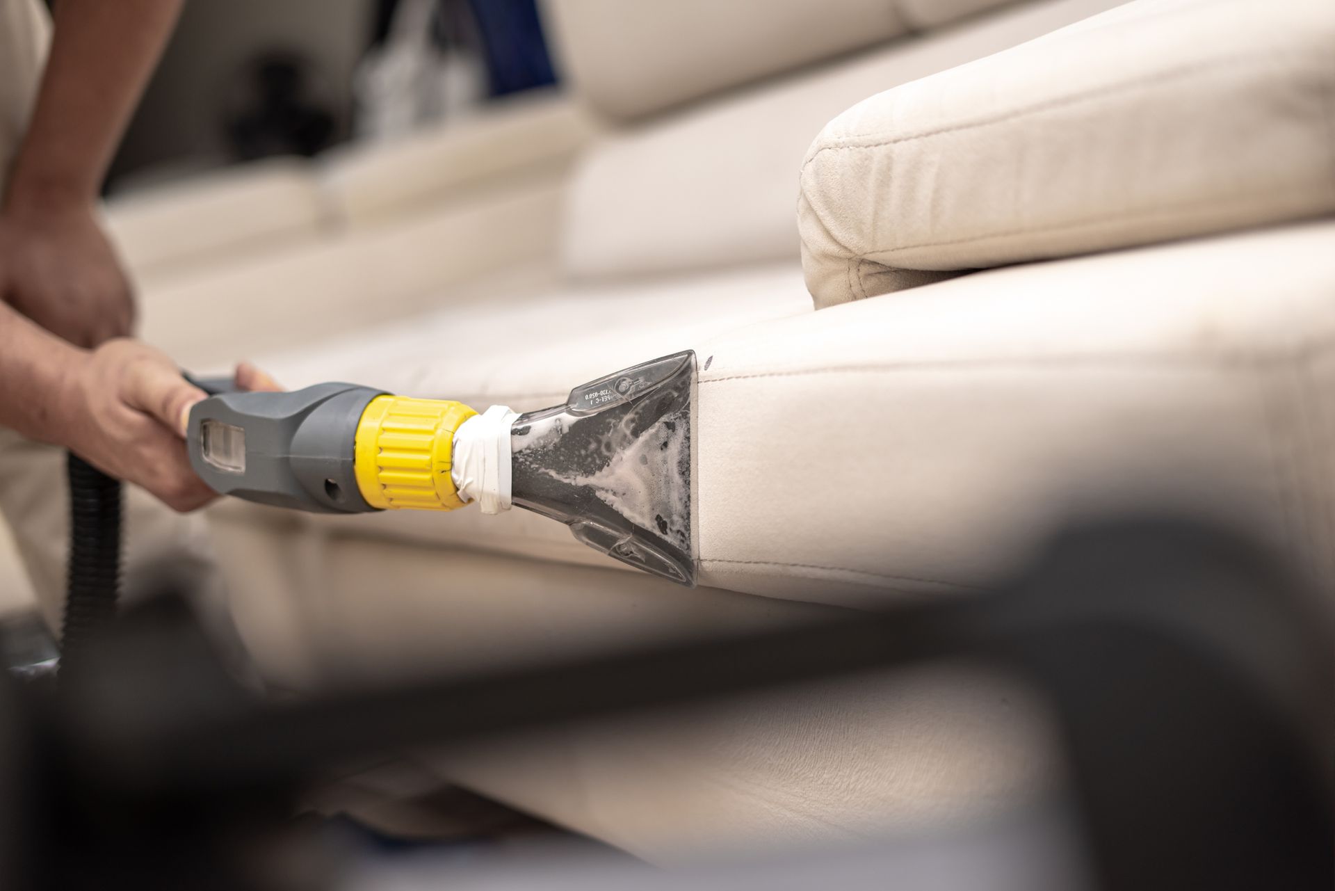 Person cleaning a white couch with a professional upholstery cleaner.