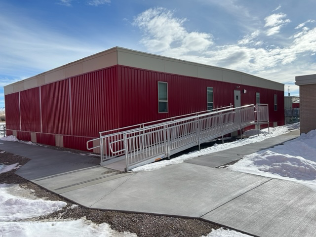 Red modular building with a ramp for accessibility; snow on the ground, sunny day.