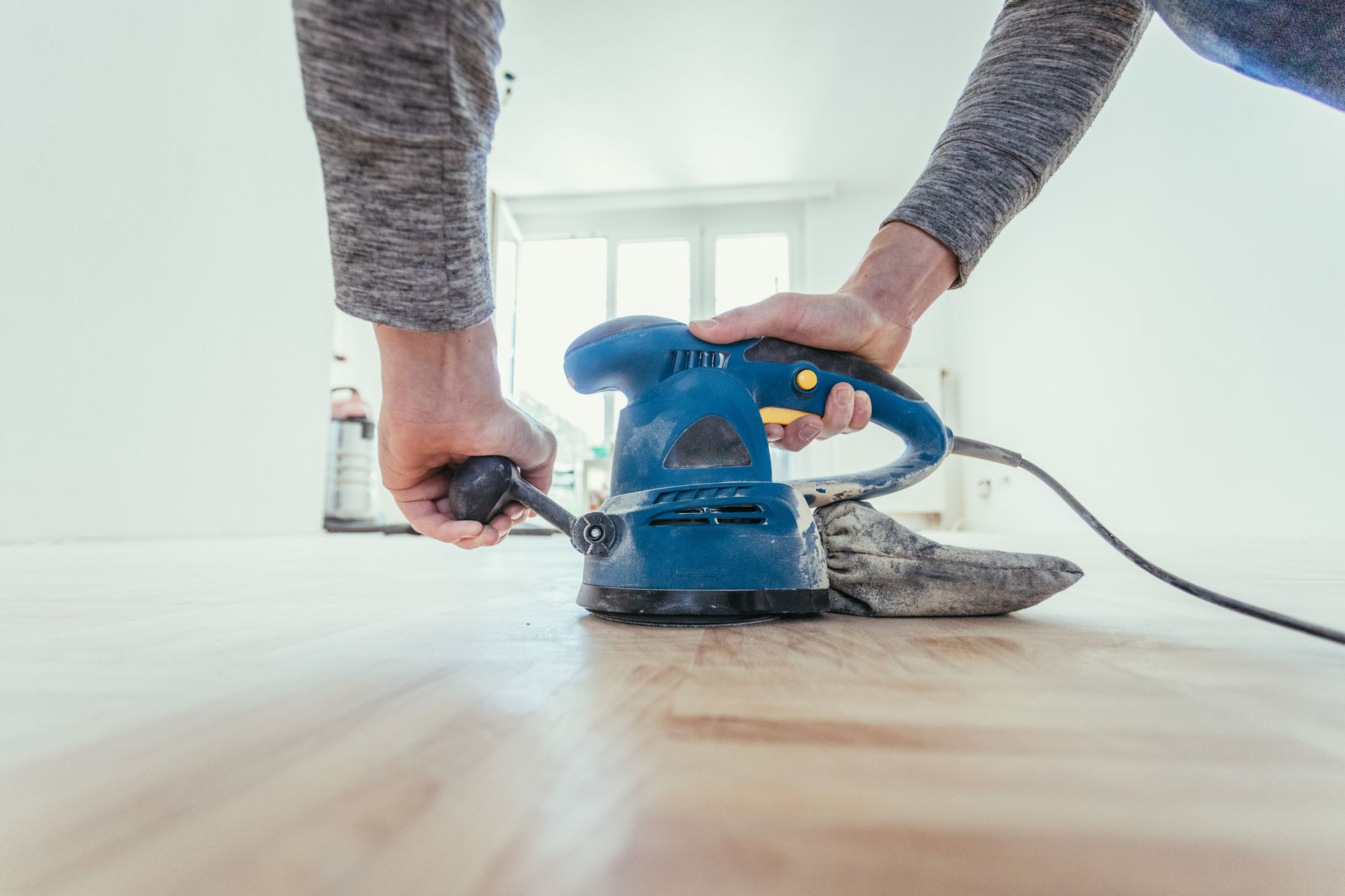 A person is sanding a wooden floor with a blue sander - Wivenhoe, TAS - Summers Floors Pty Ltd