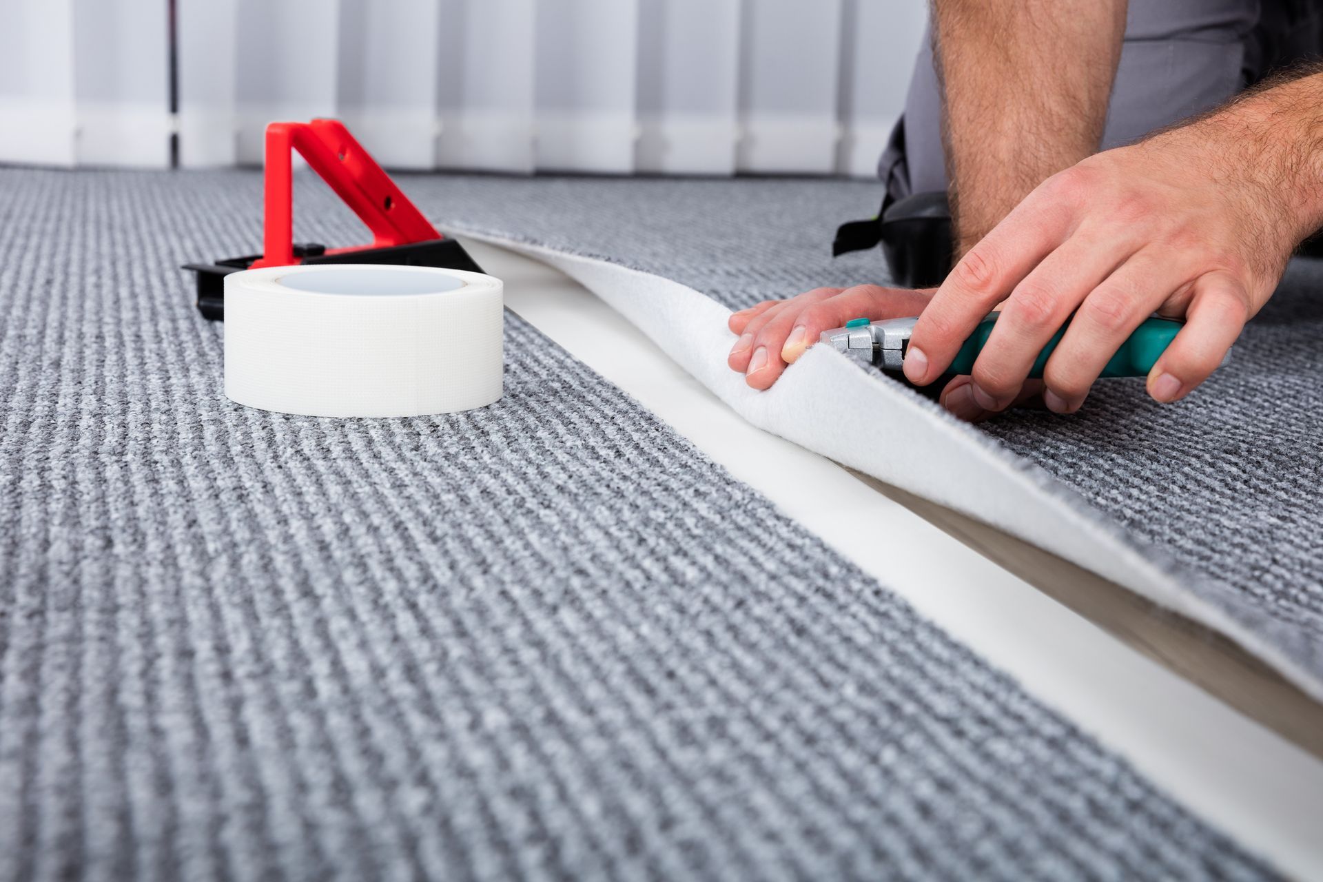 A man is cutting a piece of carpet with a pair of scissors - Wivenhoe, TAS - Summers Floors Pty Ltd