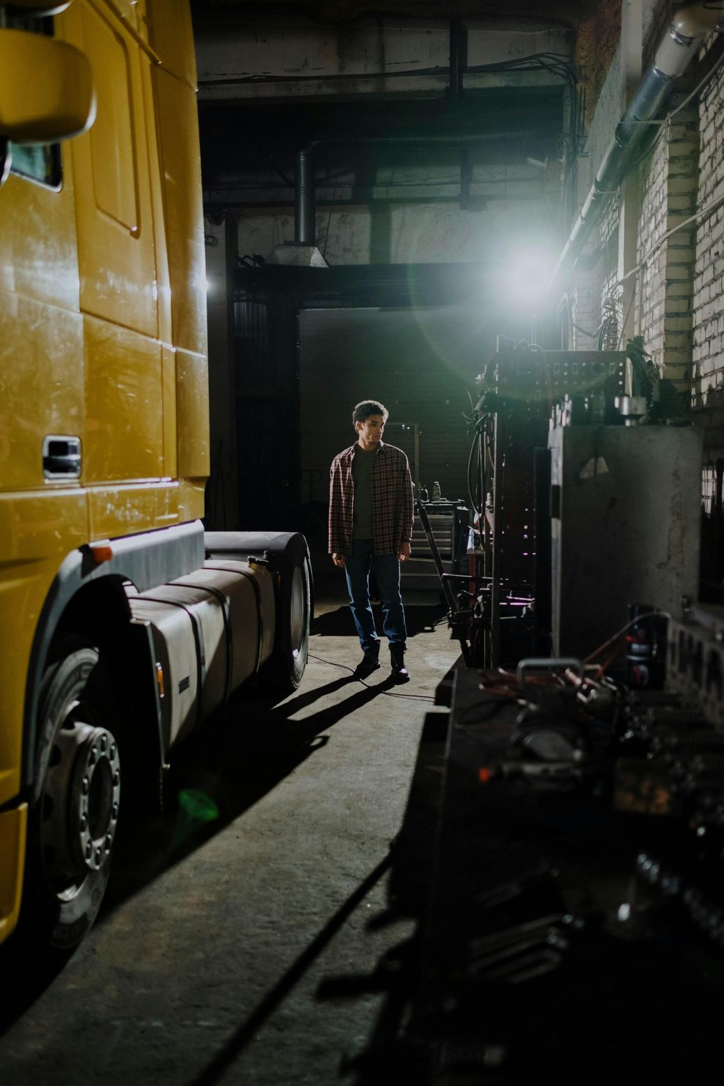 A man is standing next to a yellow semi truck in a garage.