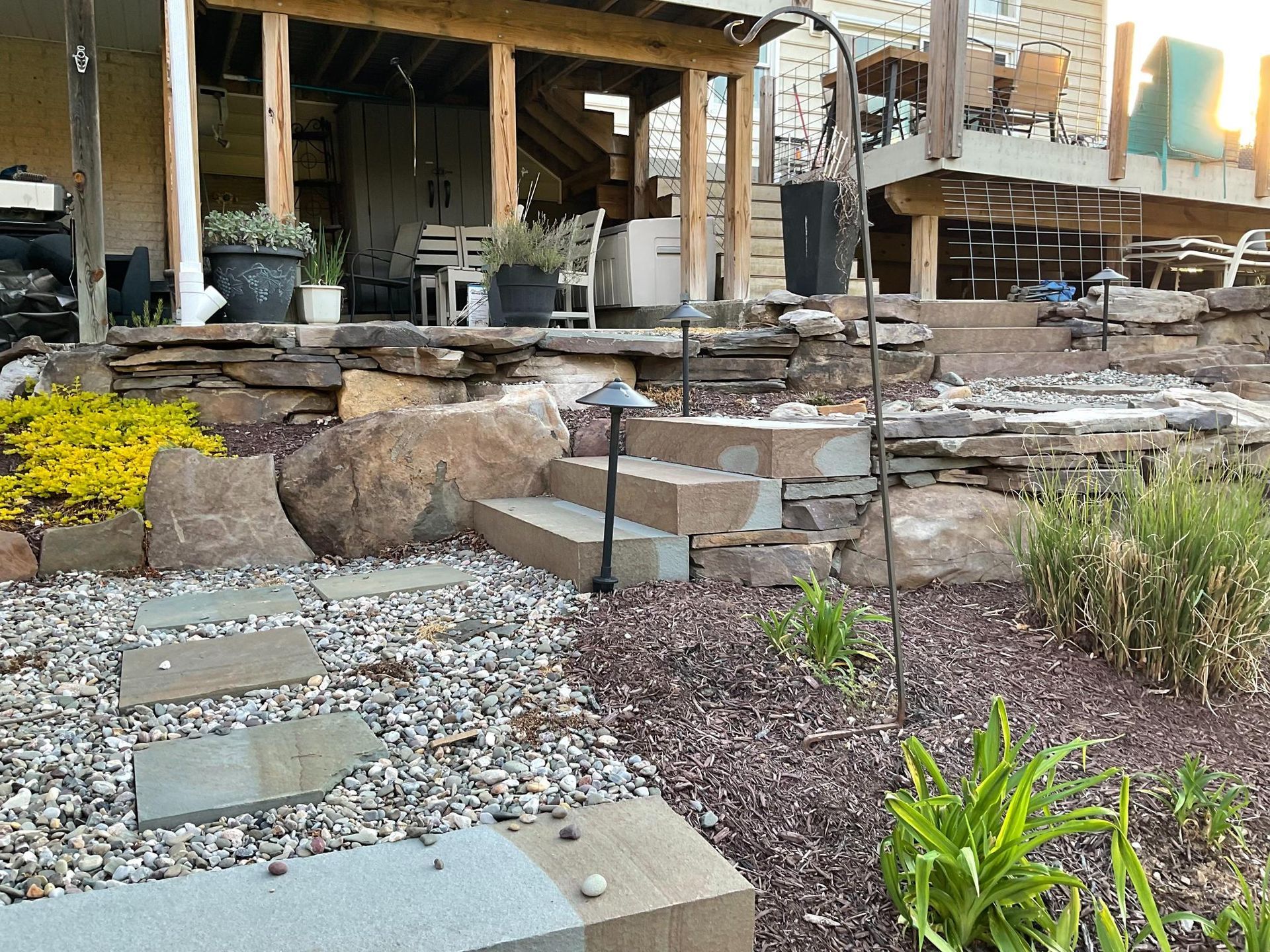 An ornate black iron gazebo with a blank screen stands in a lush, green public park with manicured landscaping.