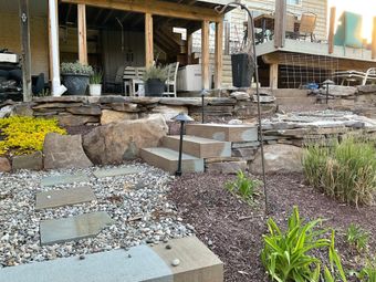 A black metal fence stretches across a green backyard lawn, with trees and a house visible in the background.