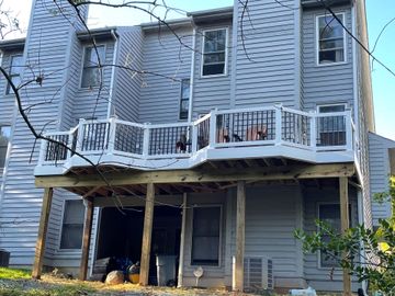 A wooden deck featuring a dining table, chairs, and potted plants next to a screened-in porch and a house.