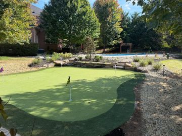 A swimming pool patio with landscaped mulch beds bordered by grey stones, leading toward a small white shed in the yard.