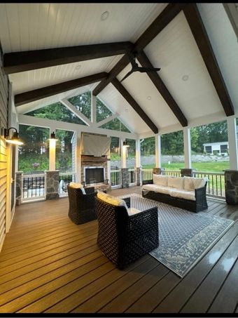 A high-angle view of a patio with a hot tub, small swimming pool, fire pit, seating, and a pond, overlooking a grassy field.