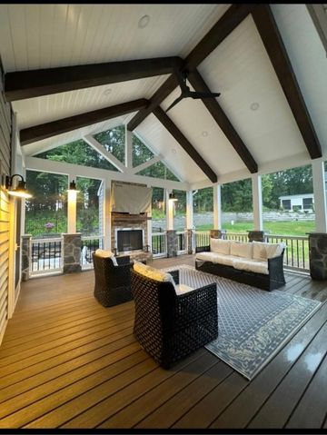 A high-angle view of a patio with a hot tub, small swimming pool, fire pit, seating, and a pond, overlooking a grassy field.