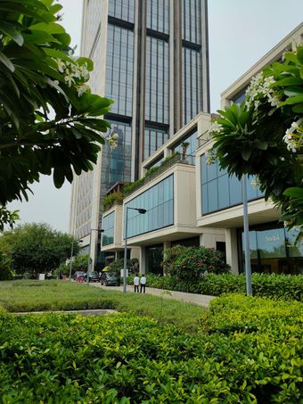 A stone patio overlooking a lush, wooded valley features a curved outdoor sectional, fire pit, chairs, and lounge chair.