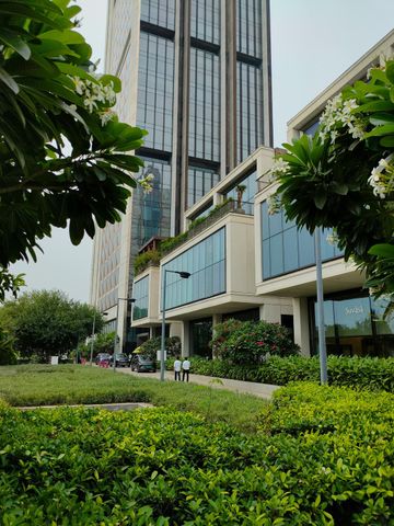 A stone patio overlooking a lush, wooded valley features a curved outdoor sectional, fire pit, chairs, and lounge chair.