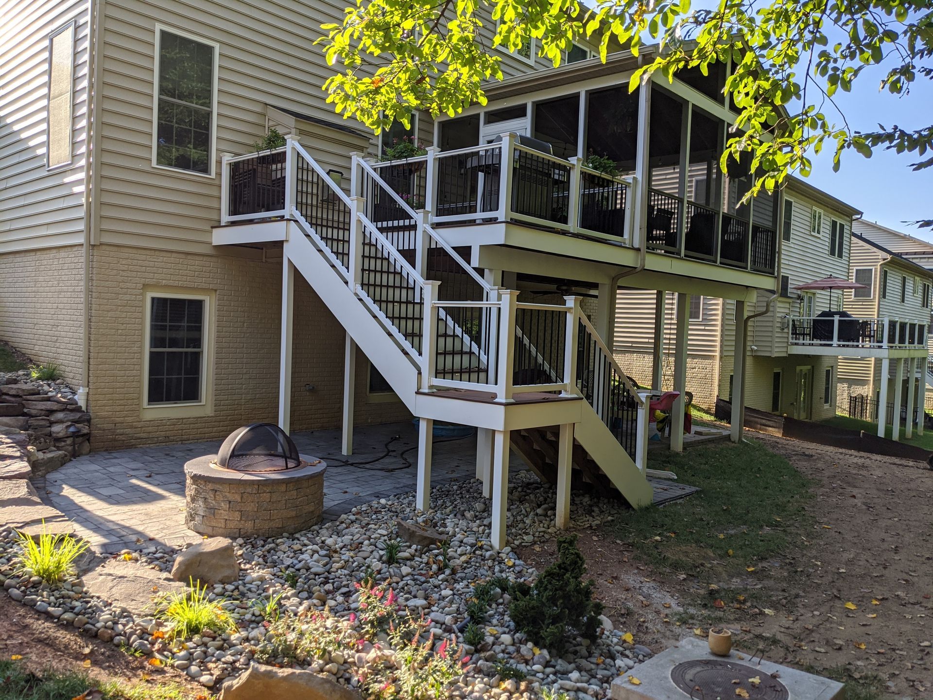 A multi-level backyard deck with white railings, a screened-in porch, and a stone fire pit on a patio below.
