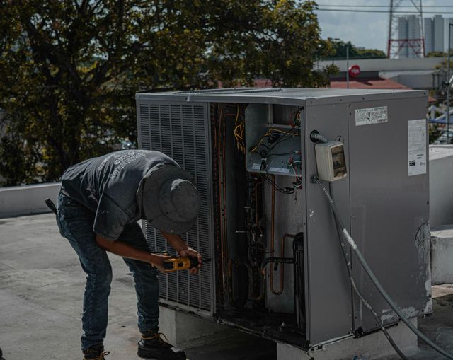 A technician repairs a large air conditioning unit on a rooftop on a sunny day.