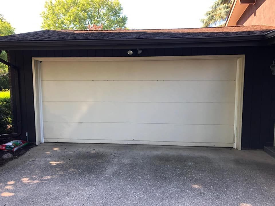A white garage door is open in front of a black house.