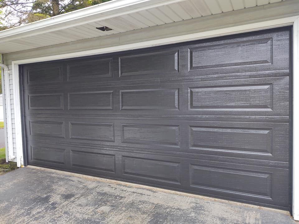 A black garage door is sitting in front of a house.