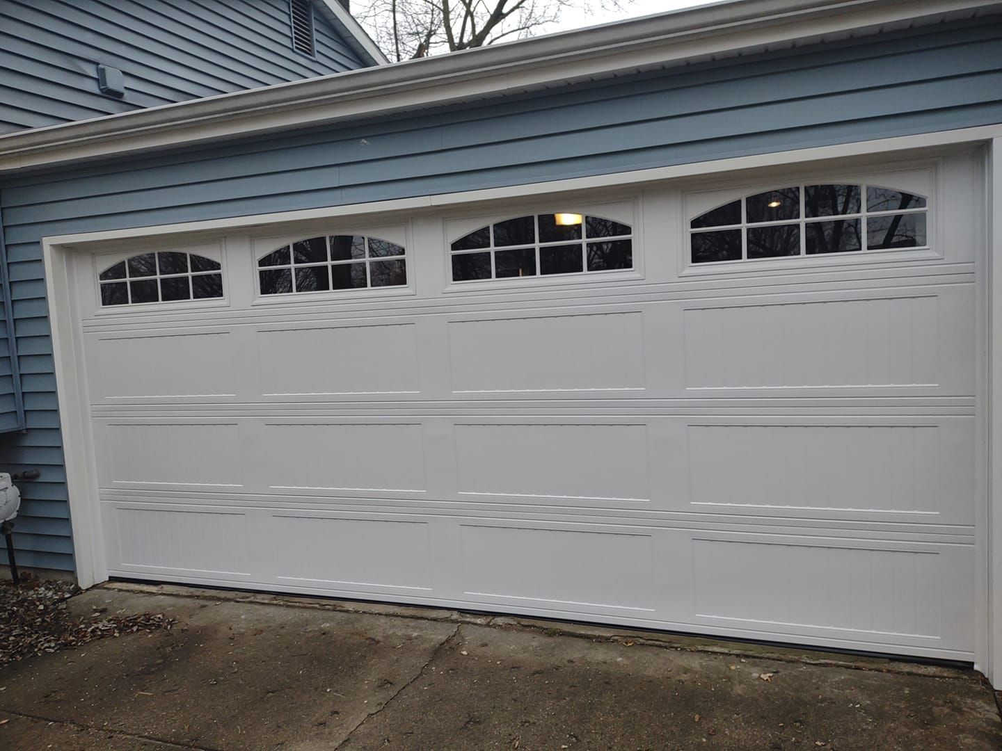 A white garage door is sitting in front of a blue house.