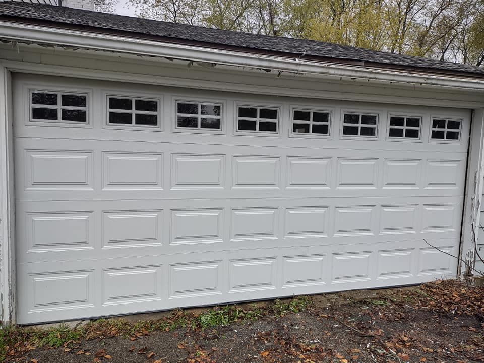A white garage door with a lot of windows is sitting next to a house.