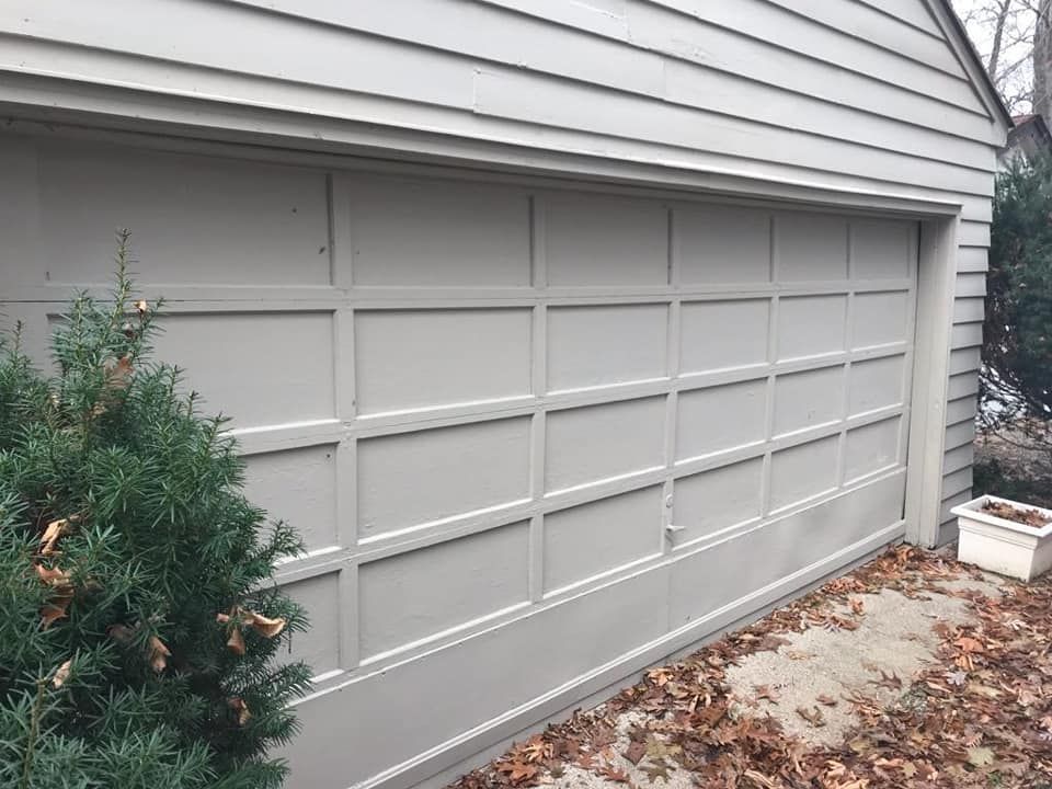 A gray garage door is sitting on the side of a house.