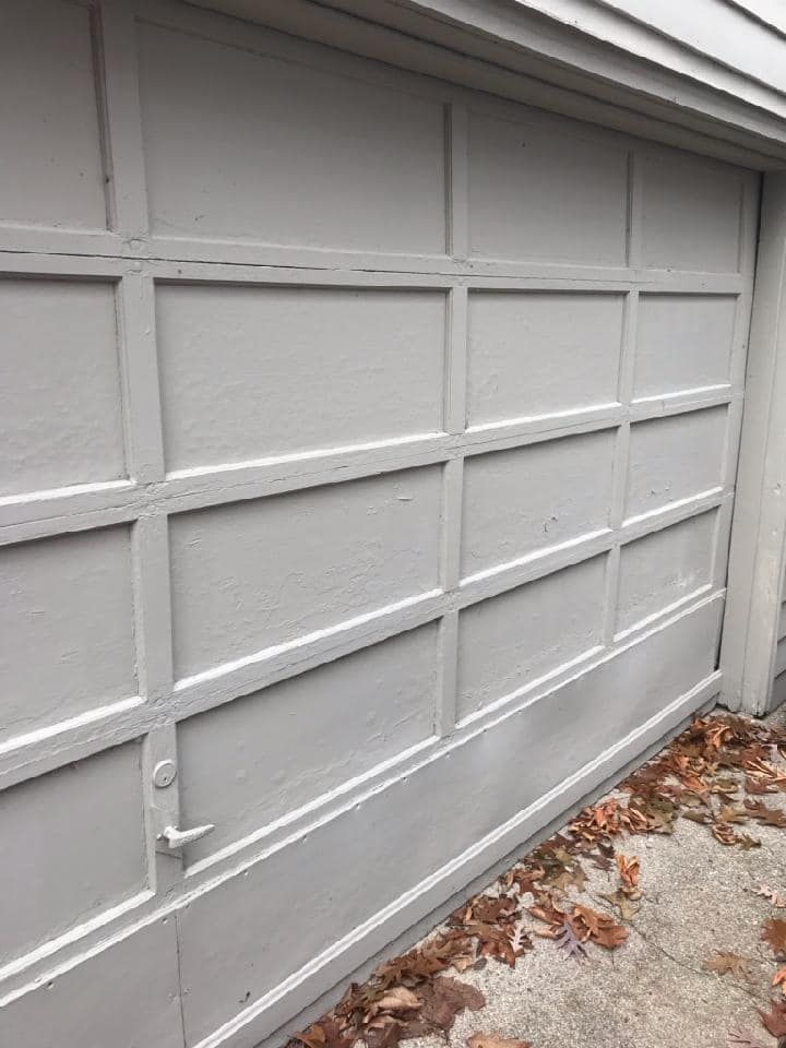 A close up of a white garage door with leaves on the ground.