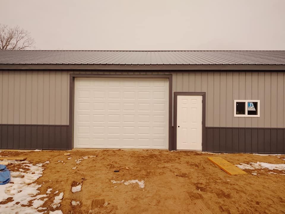 A building with a garage door and a window is sitting in the dirt.