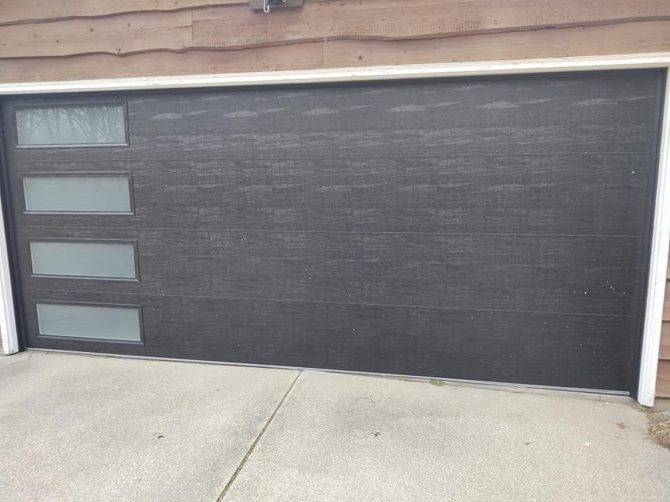 A black garage door with three windows is sitting on the side of a house.