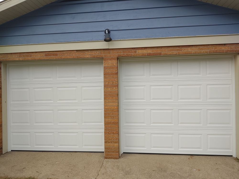 Two white garage doors on a house with a blue siding