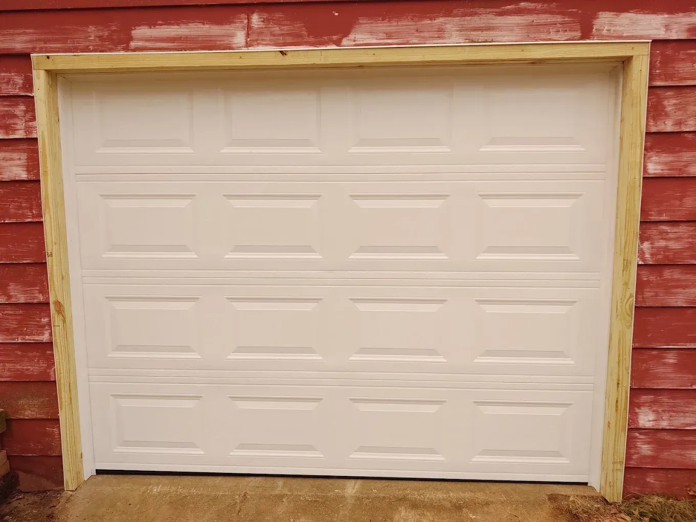 A white garage door is sitting in front of a red building.
