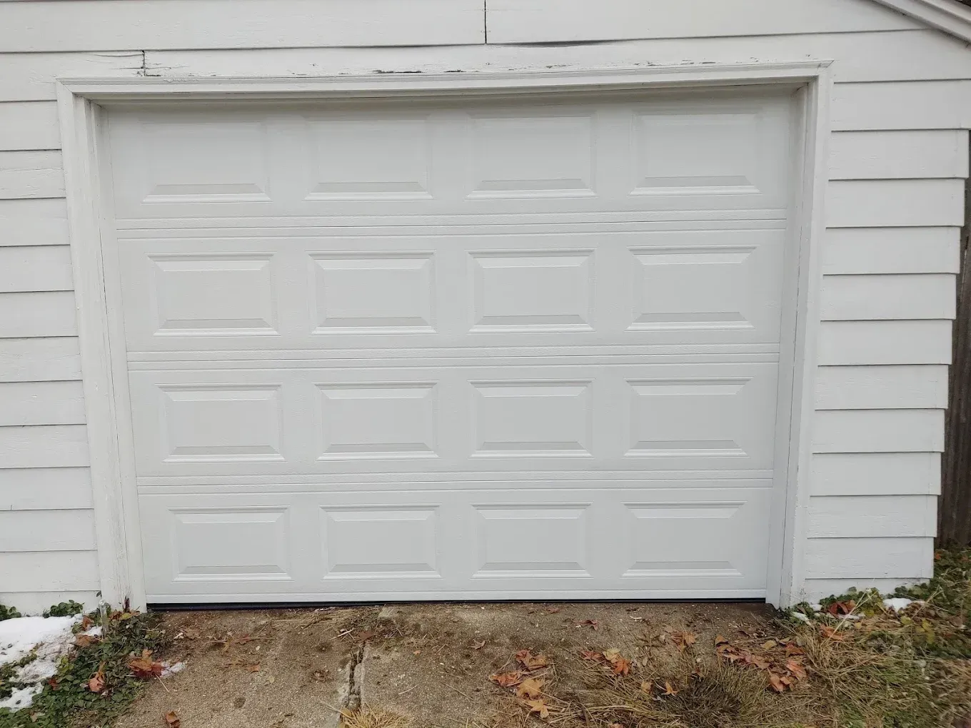 A white garage door is sitting in front of a white house.