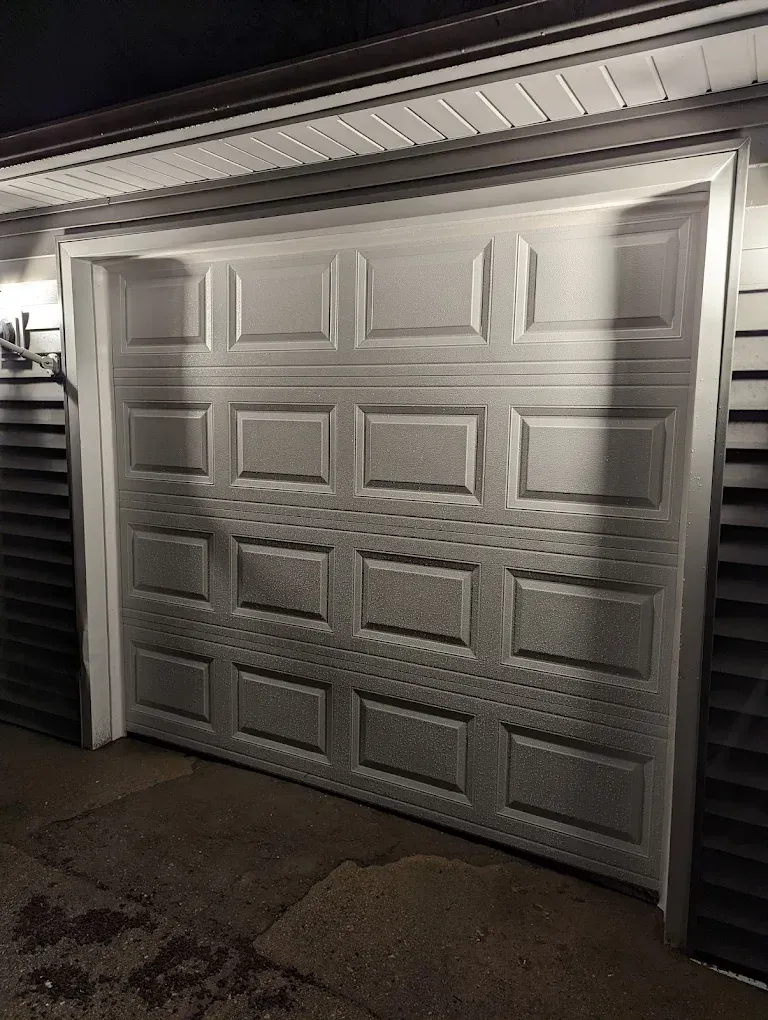 A white garage door is open in front of a house at night.