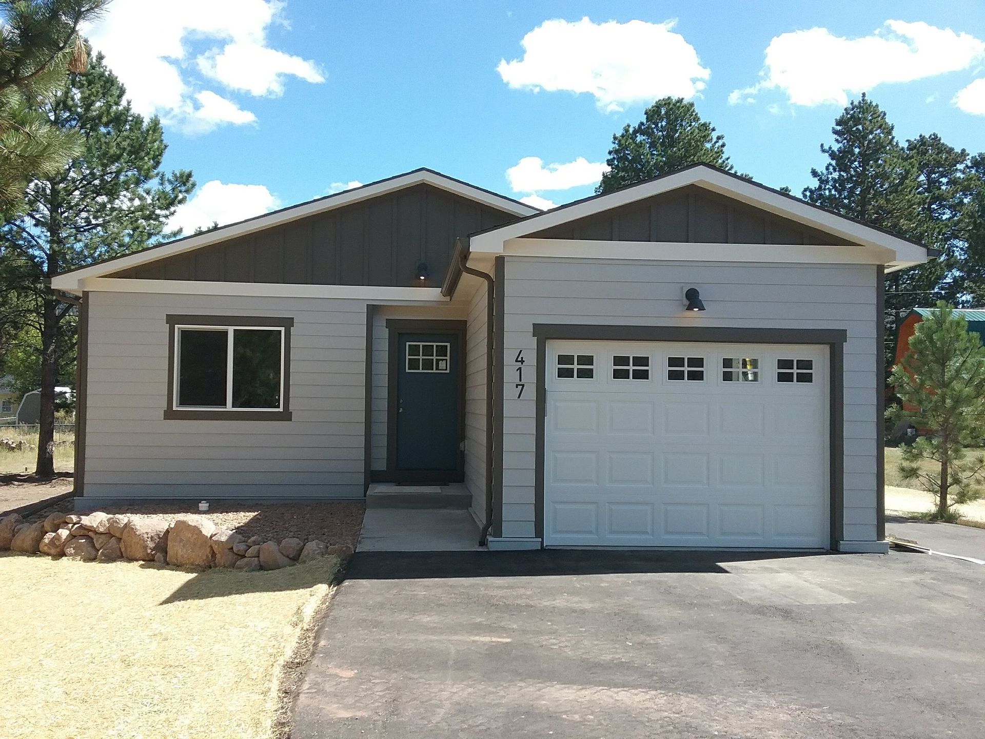Gray ranch-style house with a white garage door, dark door and trim, on a paved driveway with landscaping.