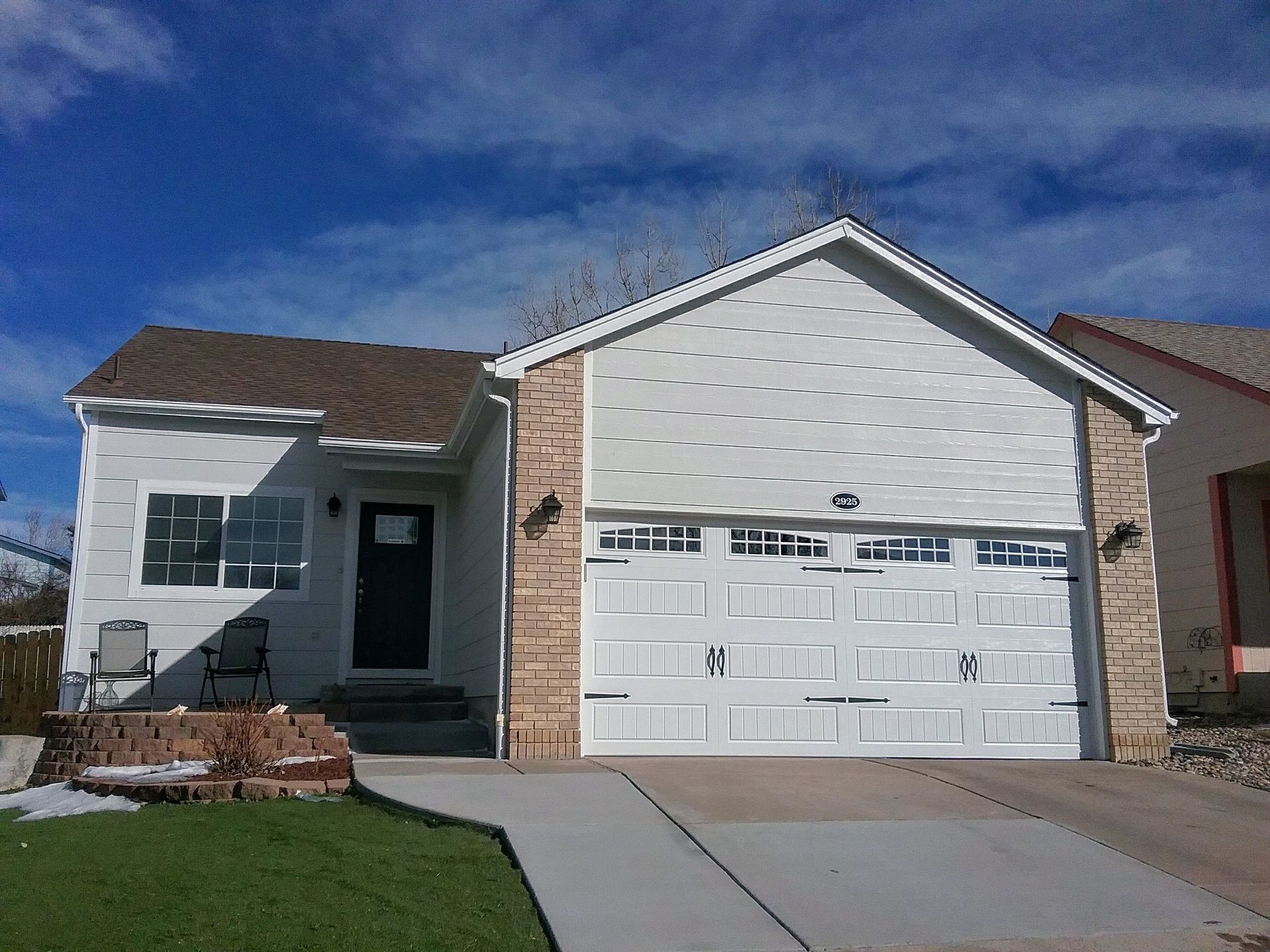 White house with a garage, tan stone accents, and a blue sky.