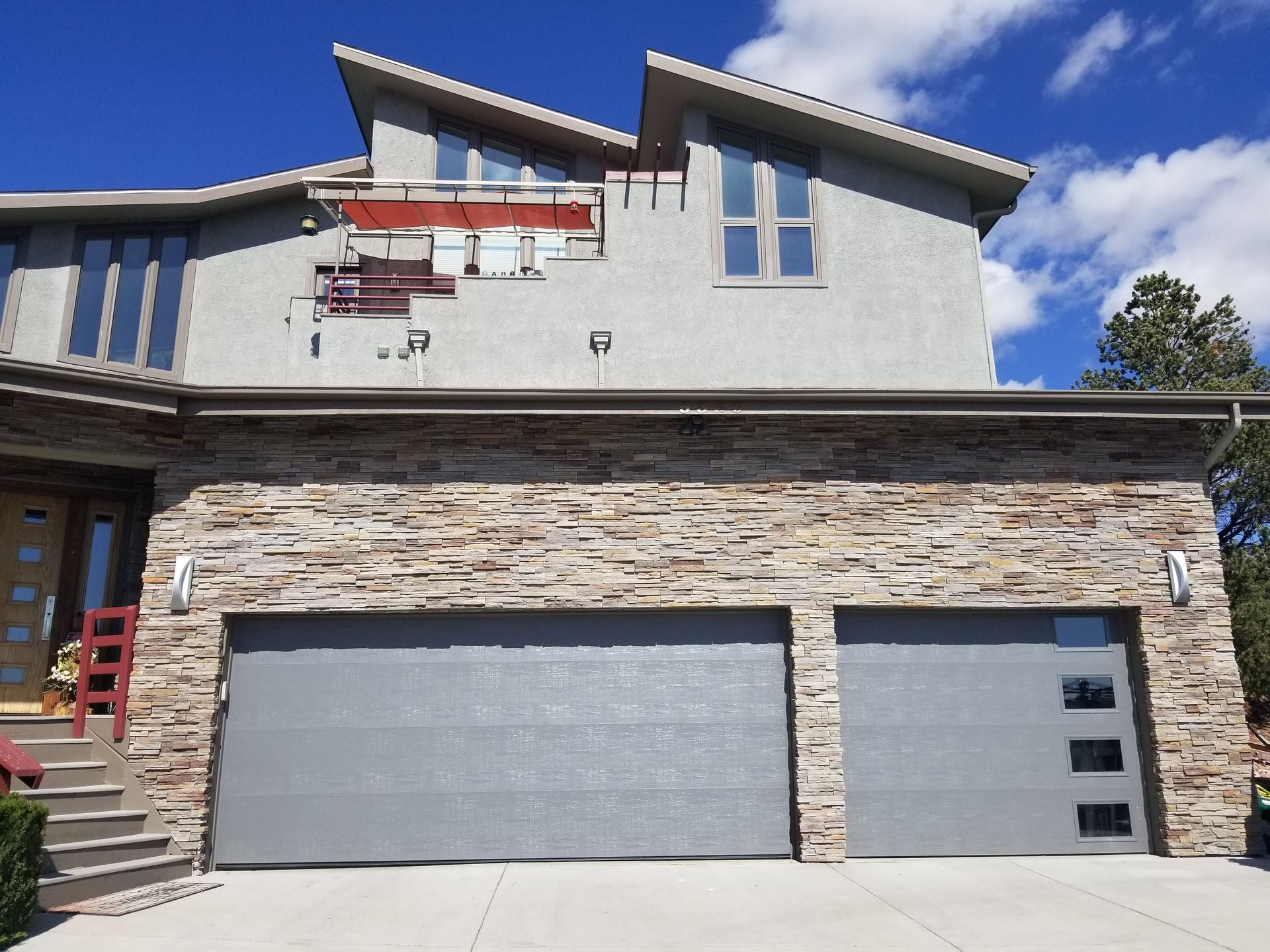 Two-story house with gray garage doors and stone facade. Blue sky background.