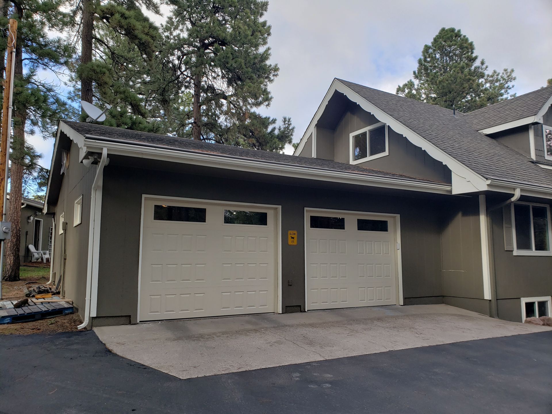 Two-car garage with white doors, gray exterior, and dark driveway under a roof.