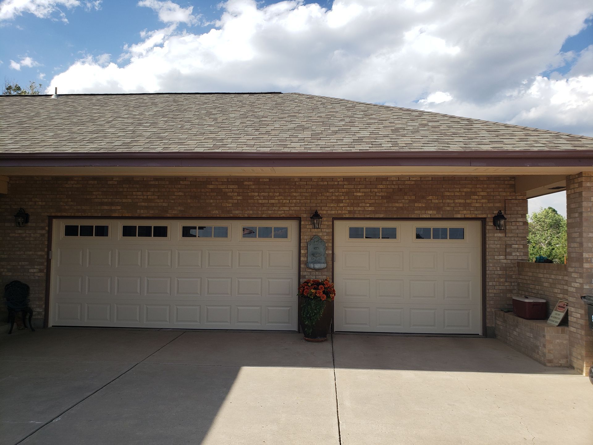 Tan brick garage with two white garage doors, brown roof, and concrete driveway.