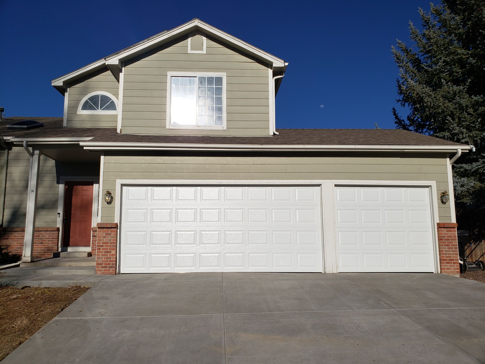 Two-story house with white garage doors and a concrete driveway on a sunny day.