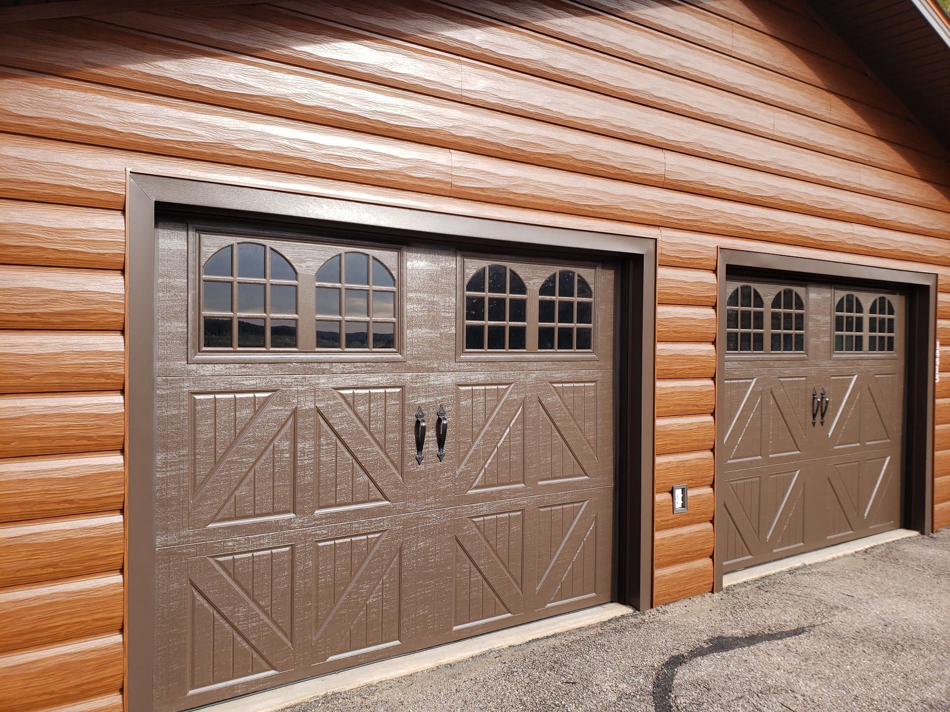Two brown garage doors with arched windows set in a brown log-sided building.