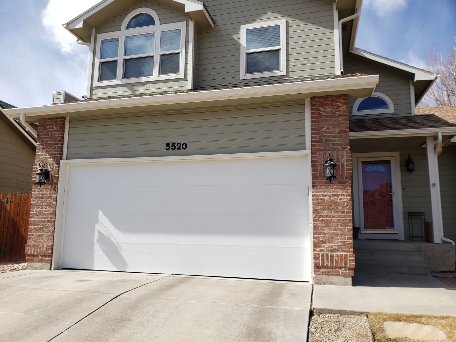 Two-story house with a white garage door, red brick accents, and a red front door.