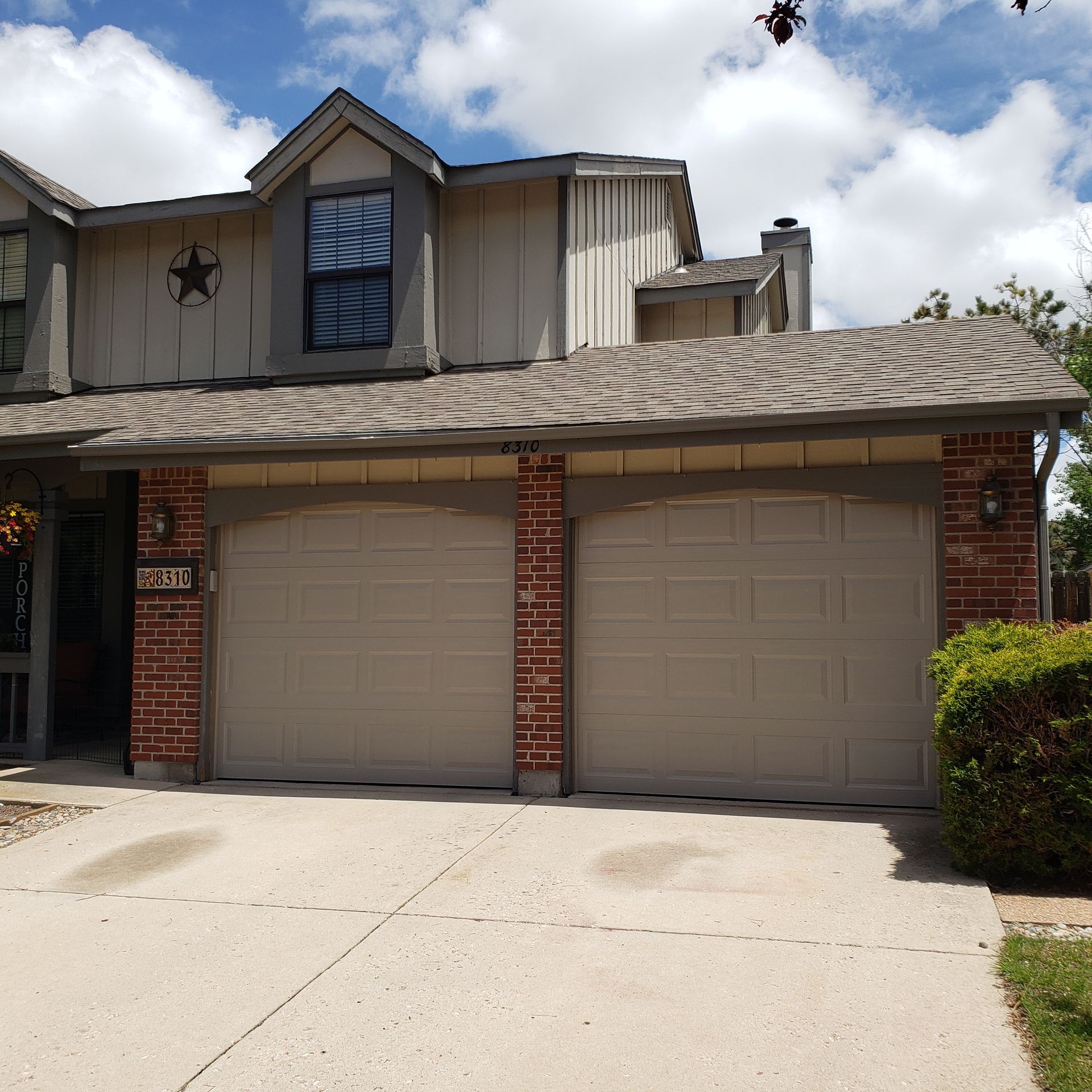 Two-story house with tan garage doors, brick accents, and a driveway on a sunny day.