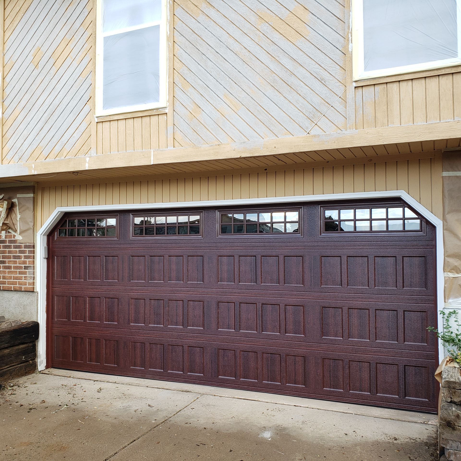 Brown garage door with windows, on a beige house.