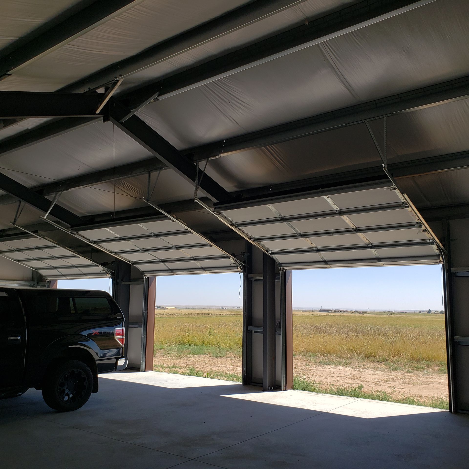 Interior view of a metal building with open doors; a black truck is parked inside.