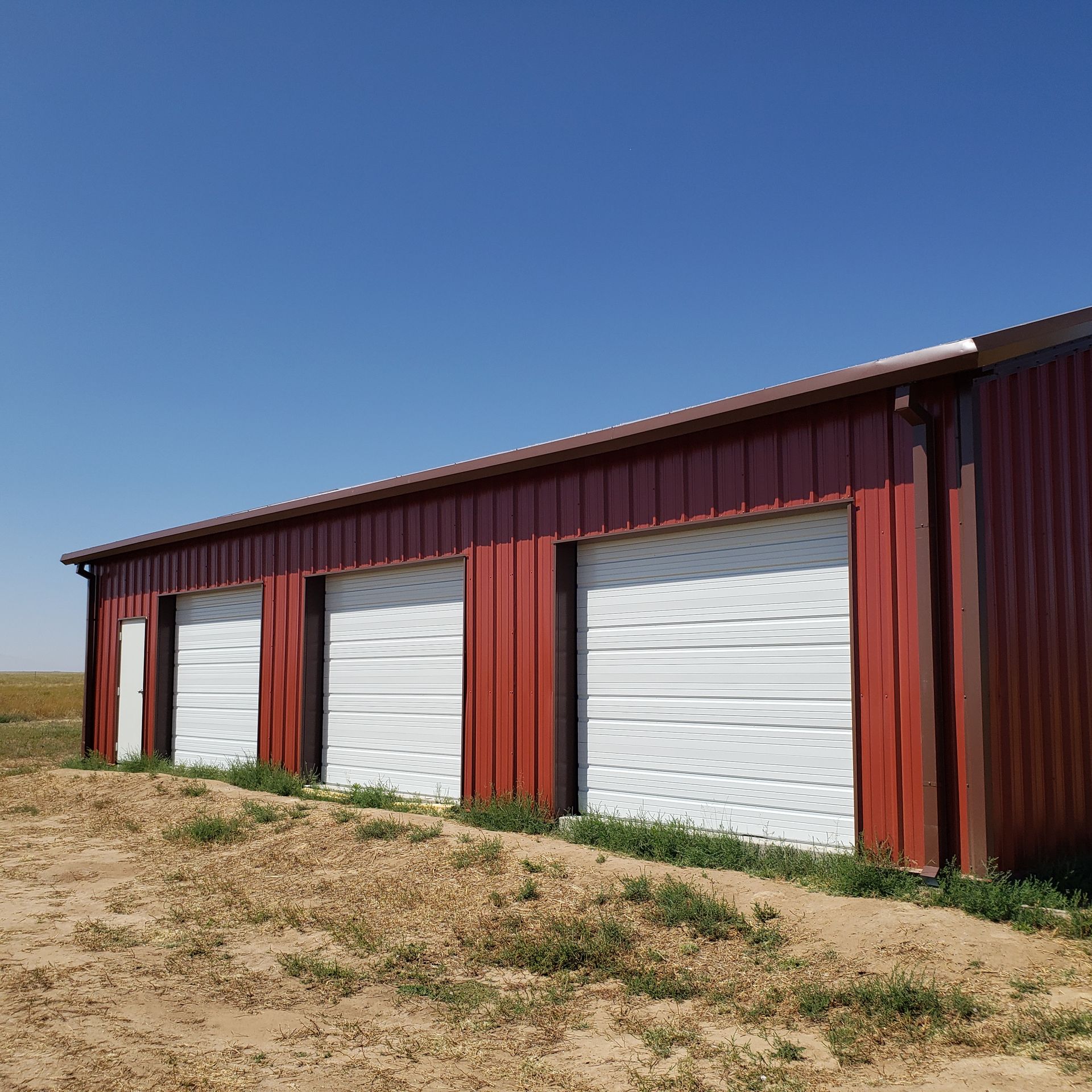 Red metal building with white garage doors against a clear blue sky.