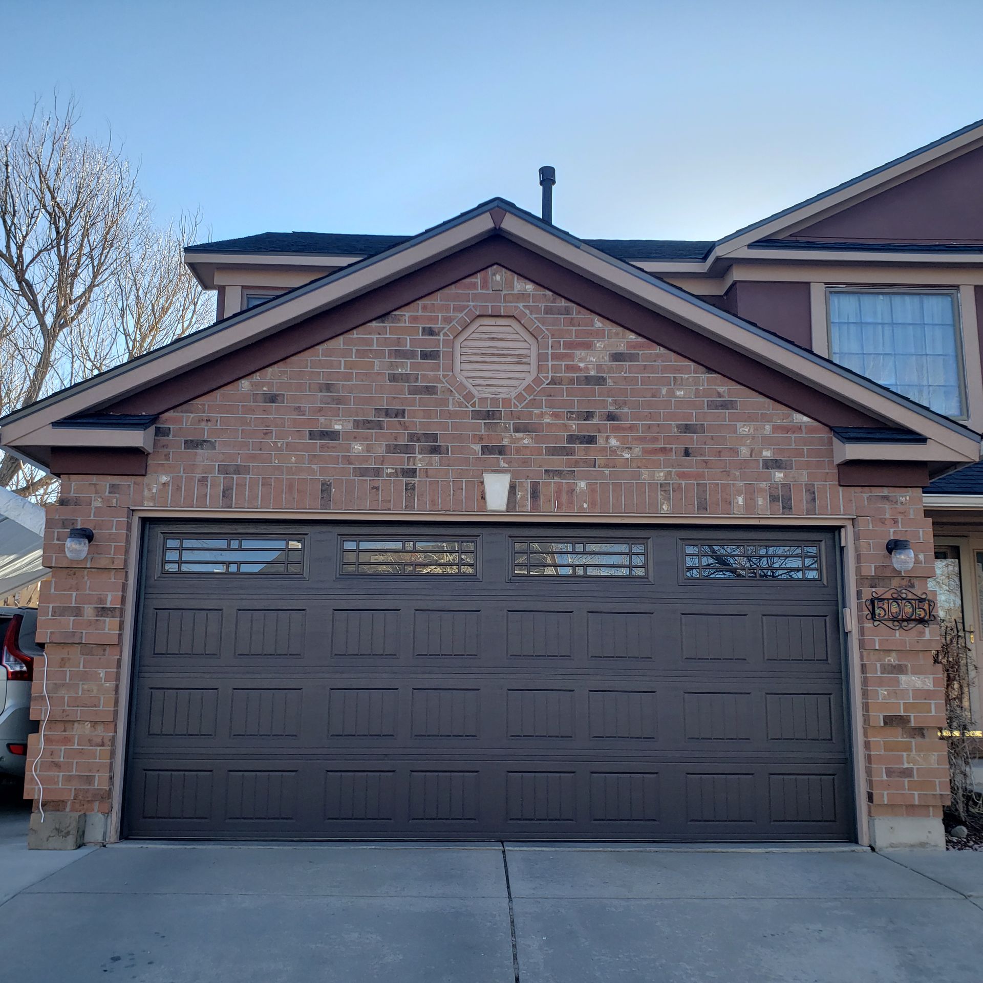 Brown garage door on a brick house with an attached driveway, under a clear sky.