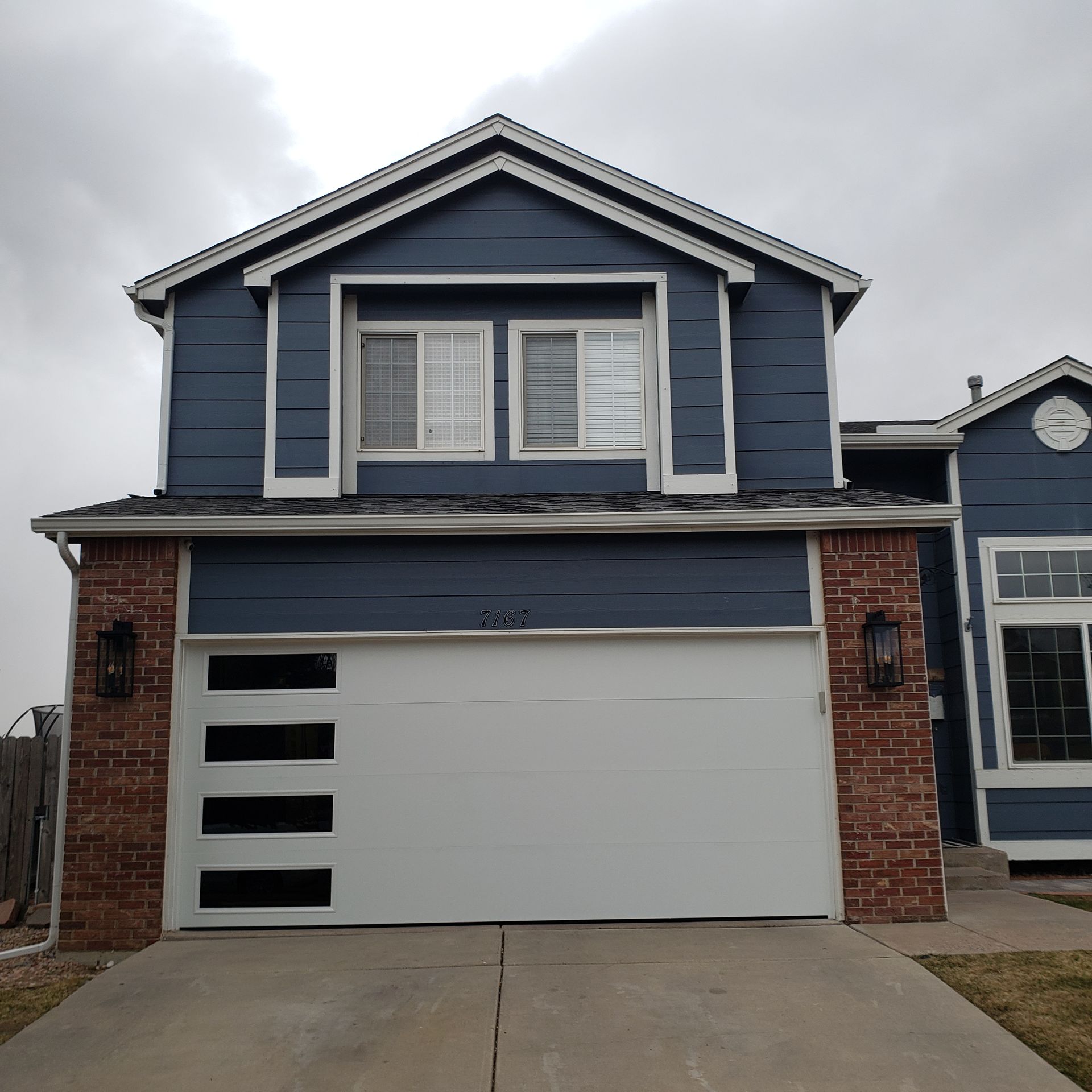 Two-story house with a blue exterior and a white garage door; brick accents.