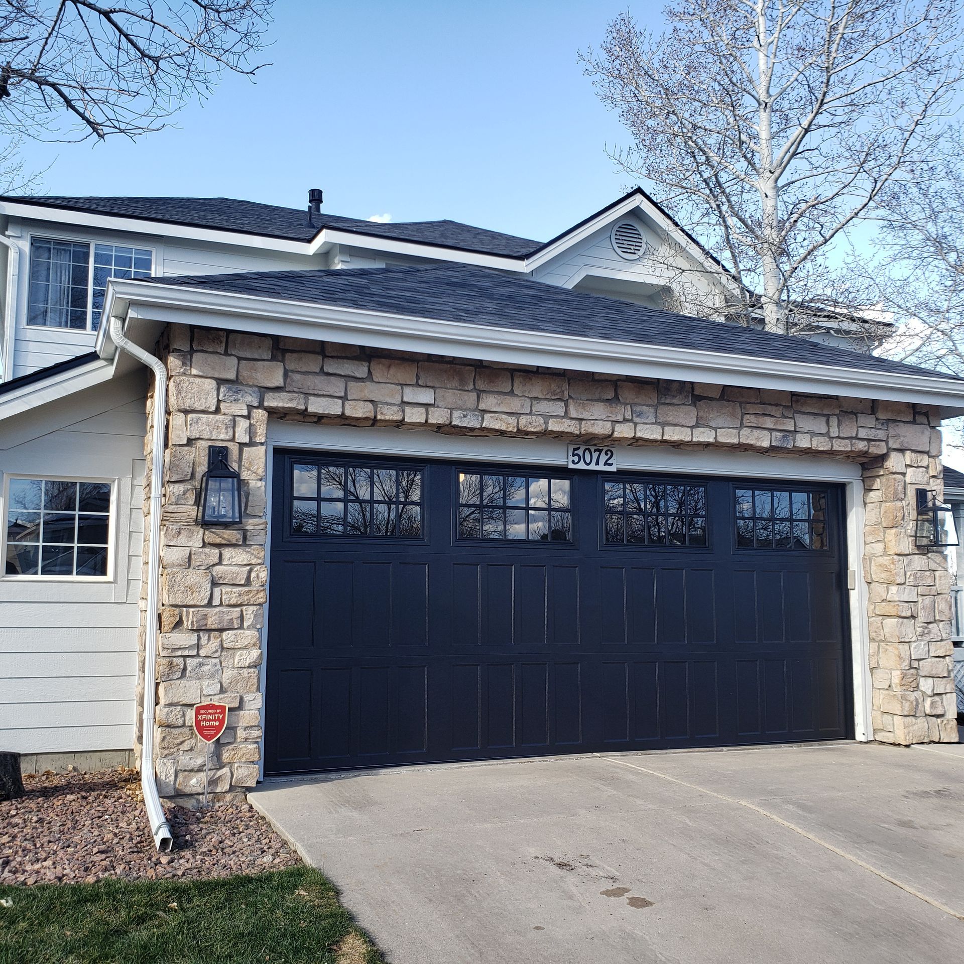 Black garage door with stone trim on a two-story house.