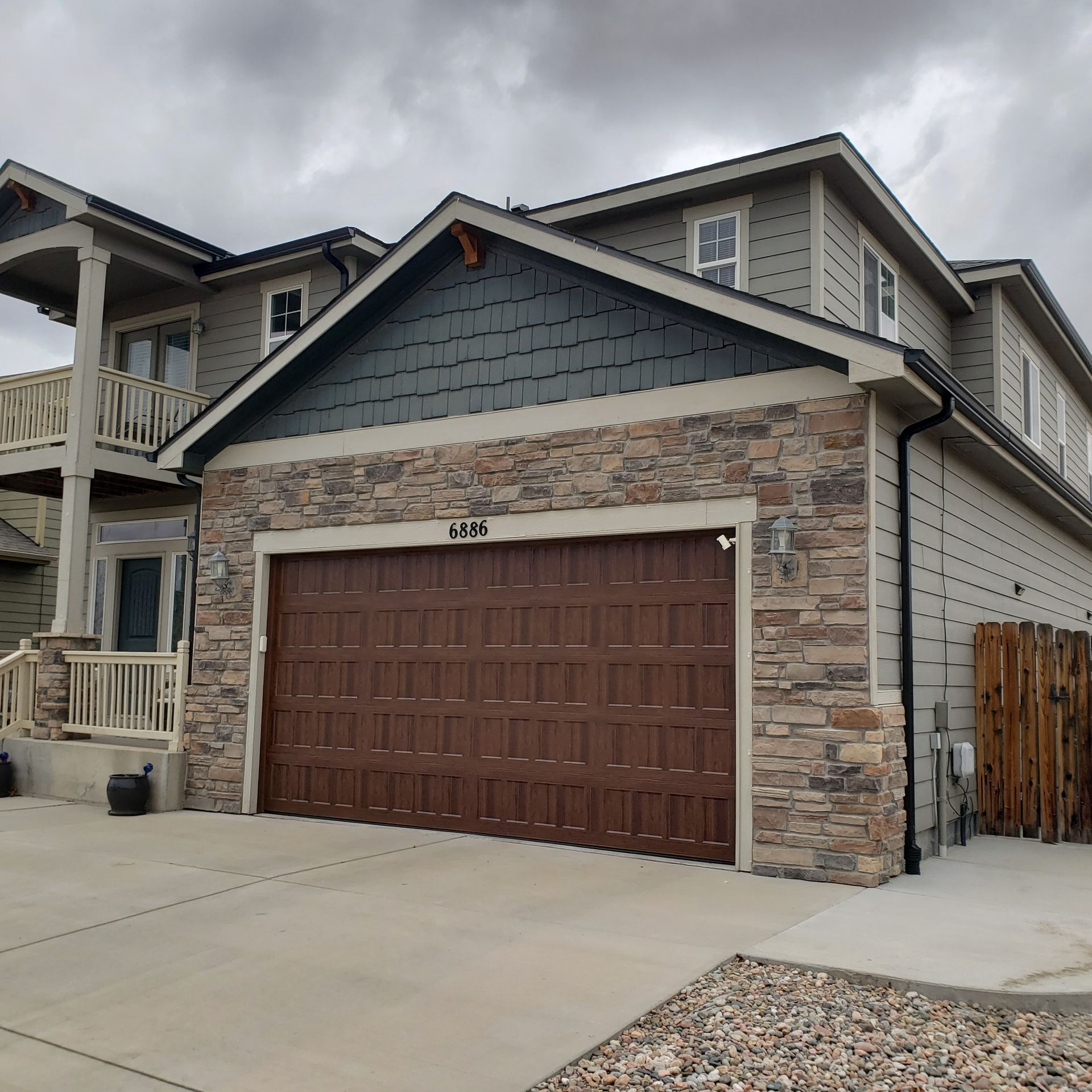 House with brown garage door, stone facade, and gray siding under a cloudy sky.
