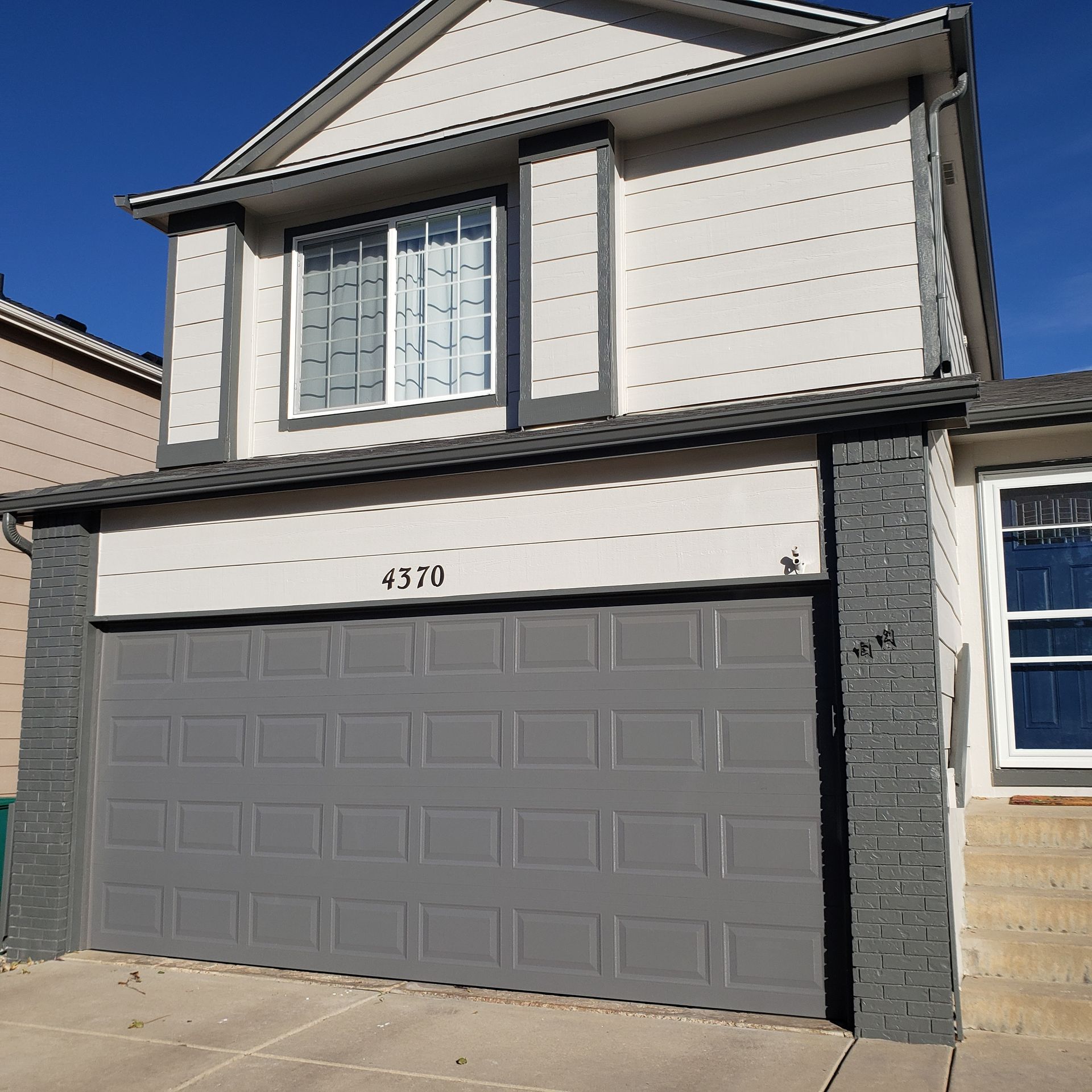 Gray two-story house with gray garage door, white windows, and brick accents. Sunny day.