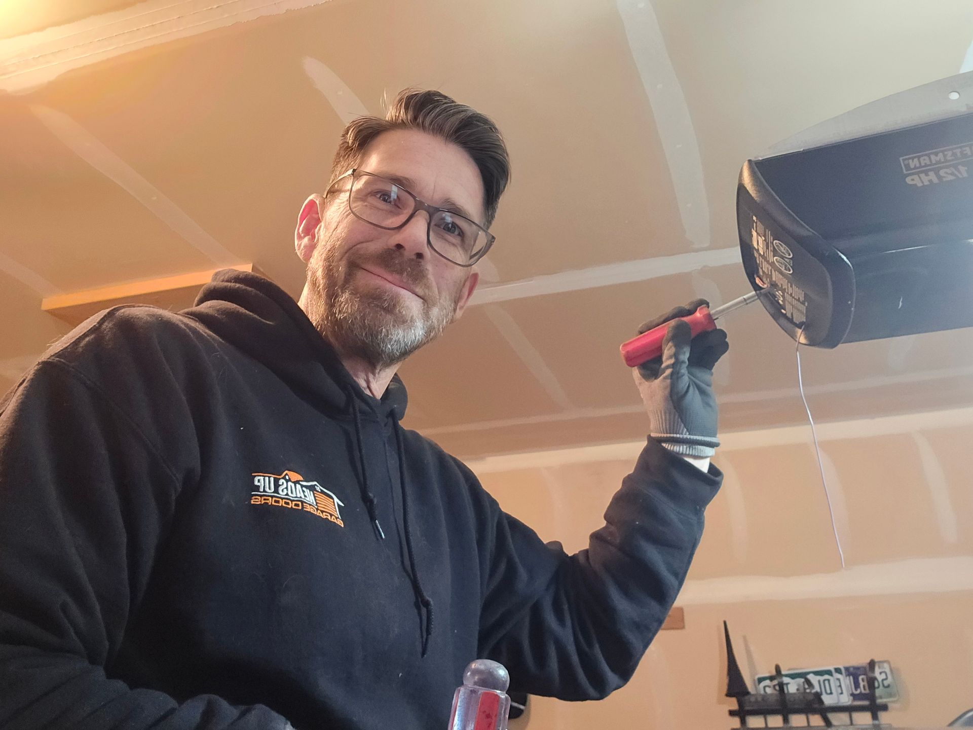 Man in black hoodie repairs garage door opener with a screwdriver.