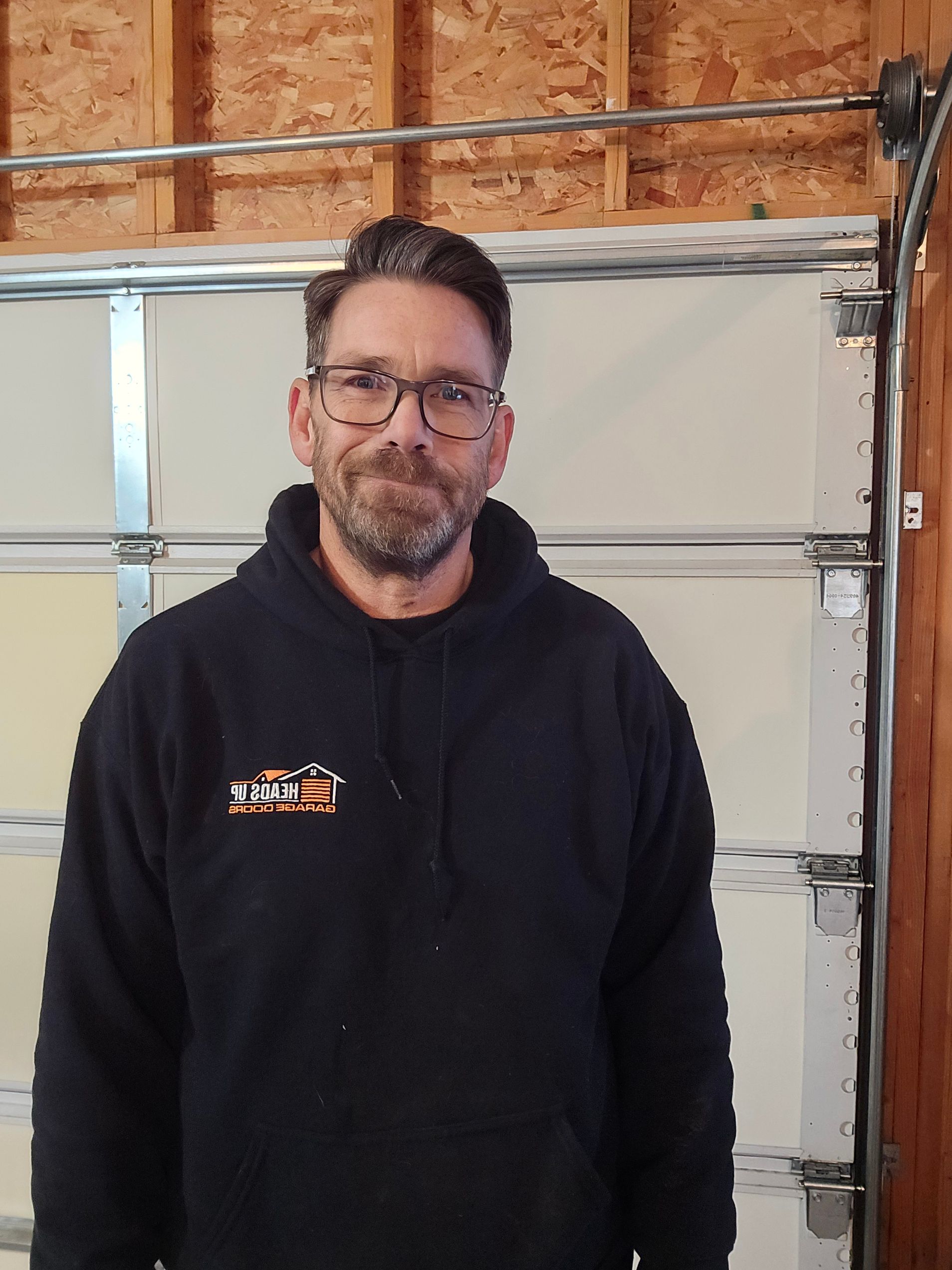 Man in black hoodie stands in front of a closed garage door.